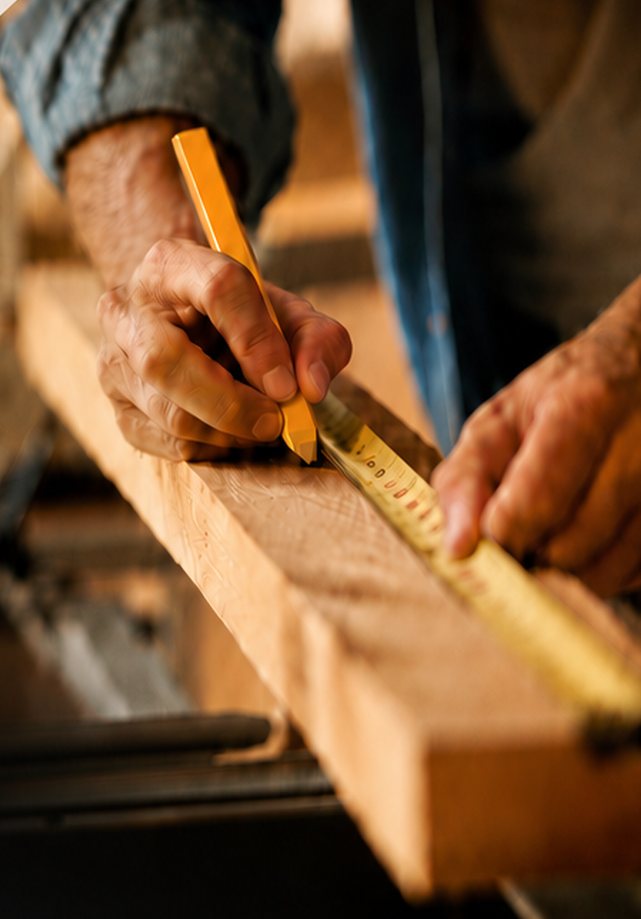 Menuisier traçant une mesure au crayon sur une pièce de bois