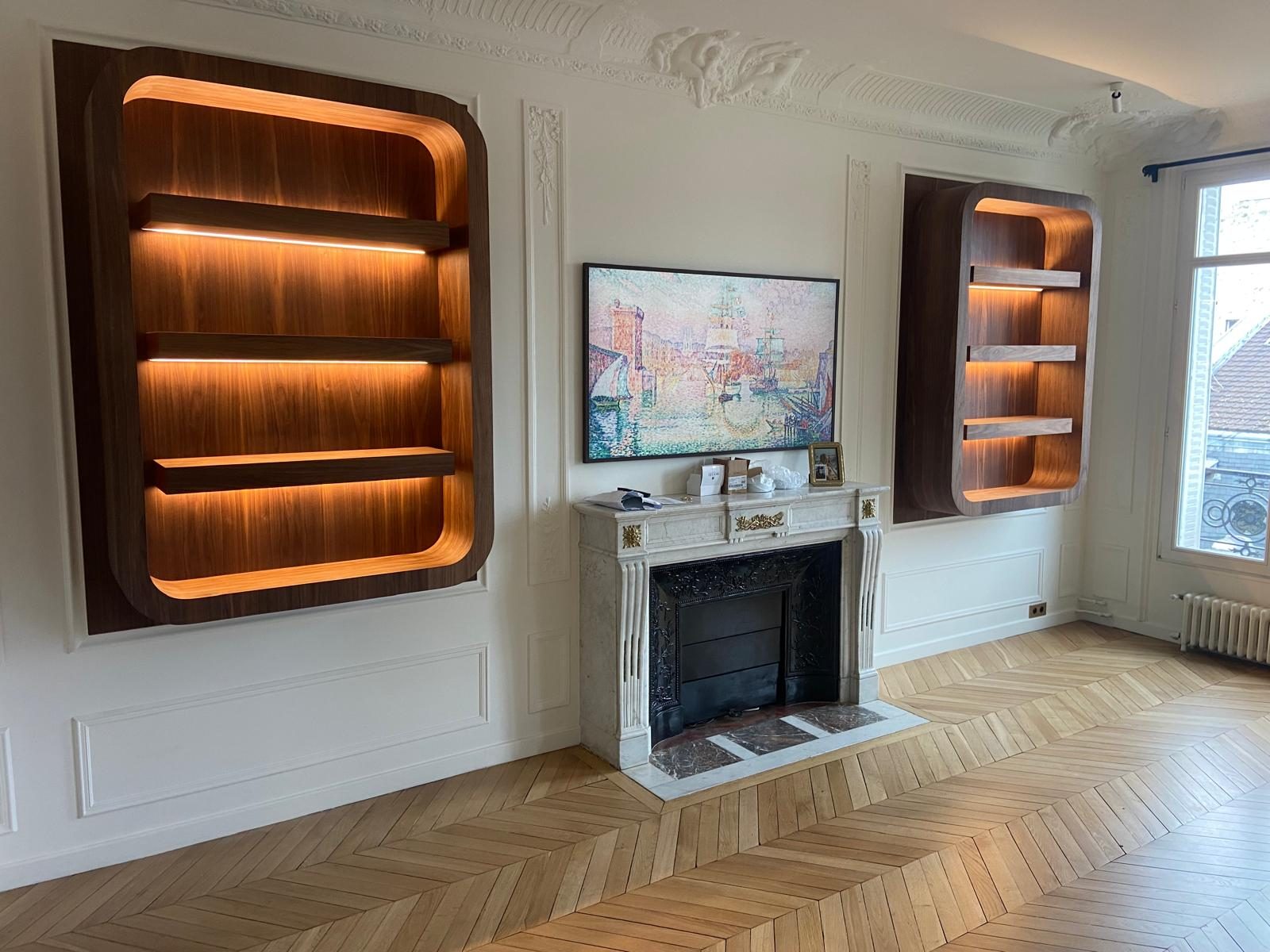 Deux bibliothèques cintrées en noyer éclairées, de part et d'autre d'une cheminée en marbre
